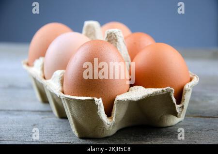 Six œufs de poulet bruns dans une boîte sur une table en bois, fond bleu Banque D'Images