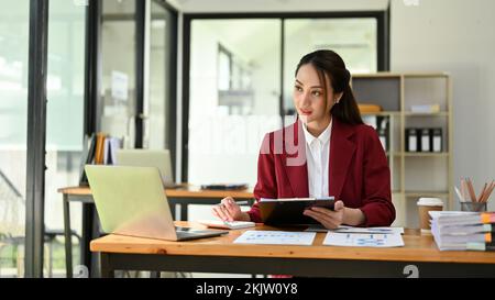 Femme d'affaires ou directrice asiatique du millénaire, professionnelle et attrayante, regardant la fenêtre, rêvant de sa réussite en travaillant chez lui Banque D'Images