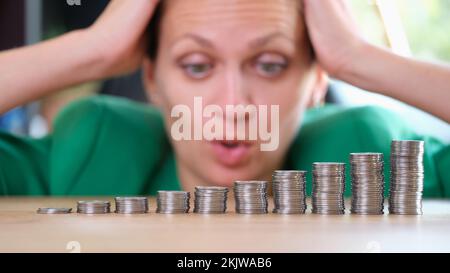 Femme choquée regardant des piles de pièces de monnaie et tenant sur la tête Banque D'Images