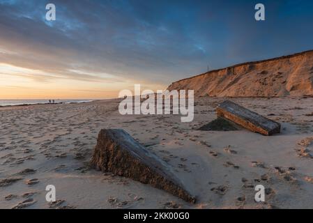 Un coup de soleil à l'aube avec des empreintes de pas dans le sable et les vieilles défenses en béton de la mer à Winterton Beach, dans Norfolk. Winterton, février 2022. Winterton, février 2022 Banque D'Images