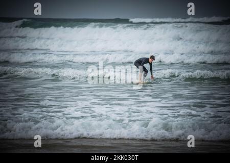 Un surfeur passe les vagues sur les mers accidentées au large de la côte ouest française près de Mimizan, en France Banque D'Images
