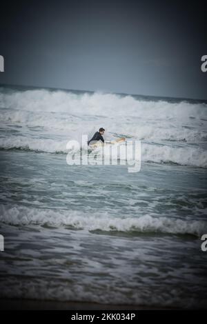 Un surfeur passe les vagues sur les mers accidentées au large de la côte ouest française près de Mimizan, en France Banque D'Images