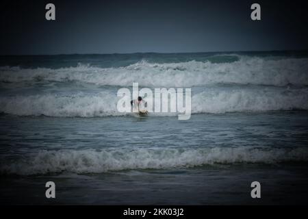 Un surfeur passe les vagues sur les mers accidentées au large de la côte ouest française près de Mimizan, en France Banque D'Images