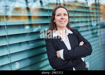 Femme d'affaires souriante se penchée devant le bureau sur un mur de verre en ville Banque D'Images