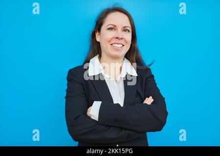 Femme d'affaires souriante avec bras croisés debout devant un fond bleu Banque D'Images