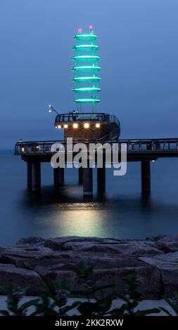 Un phare lumineux au néon sur la rive du lac Ontario, dans le parc Spencer Smith à Burlington, la nuit, avec un reflet de la lumière à la surface du lac Banque D'Images
