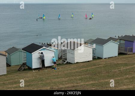 Prendre le temps de peindre et de rénover une cabane blanche sur la plage avec une nouvelle peinture sur une journée de mer calme à Whitstable parmi des huttes multicolores, belle vue sur la mer Banque D'Images