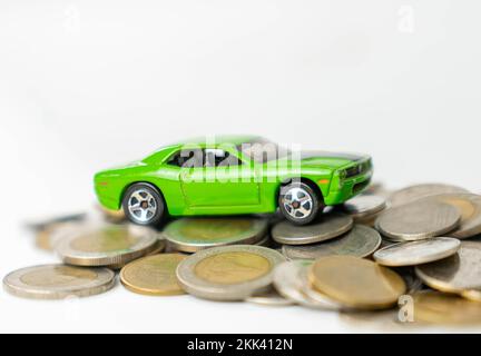 La voiture de jouet vert est sur une pile de pièces de monnaie pile , isolé sur fond blanc Banque D'Images