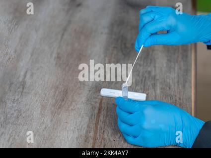Gros plan d'une main de womans effectuant un test rapide de corona ou un test d'antigène sur une table en bois. Banque D'Images
