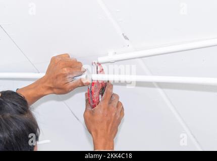 Un électricien utilise un couteau à lame pour couper un tuyau en pvc pour raccorder un tuyau dans un nouveau bâtiment. Banque D'Images