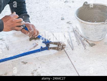 Les grosses pinces coupantes coupent la tige en fil d'acier sur le chantier de construction. Banque D'Images