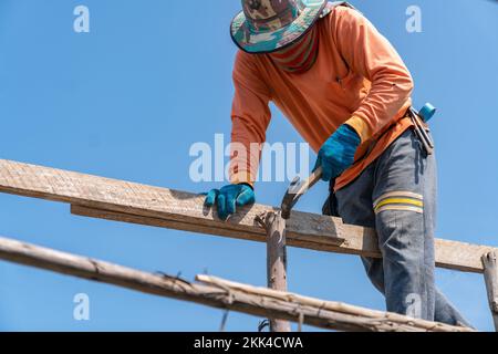 L'employé utilise des clous de marteau sur l'échafaudage pour soutenir le deuxième étage sur le chantier. Banque D'Images