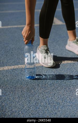 Une jogging femelle laisse la bouteille d'eau sur la piste sportive, après qu'elle ait bu Banque D'Images