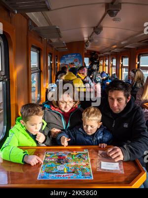 Oberwiesenthal, Allemagne. 25th novembre 2022. Les frères Leon (6, l) et Jacob (4) jouent au jeu 'Team Off!' Avec leurs parents Anja et Johannes Frei lors de la mise en service de la nouvelle voiture de jeu de Fichtelbergbahn. C'est la première voiture de jeu sur un chemin de fer étroit en Saxe. La Sächsische Dampfeisenbahngesellschaft (SDG) a investi 11 500 euros dans la conversion et la conception de la voiture. Credit: Kristin Schmidt/dpa/Alay Live News Banque D'Images