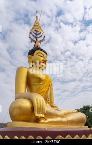 Vue latérale à angle bas de la statue de bouddha d'or assise sur le ciel bleu avec des nuages à l'ancien temple bouddhiste de Wat Chiang Yuen, Chiang Mai, Thaïlande Banque D'Images