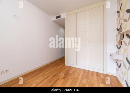 Chambre avec une armoire intégrée avec trois portes en bois blanc, des murs parés et du parquet en chêne français Banque D'Images