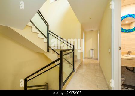 Escalier intérieur de maison individuelle avec sol en marbre crème, balustrade en métal et en verre et murs jaune pâle Banque D'Images