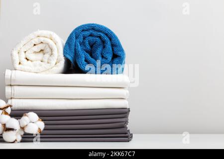 Une pile de linge de lit, des rouleaux de serviettes bleues et blanches sur la table. Banque D'Images