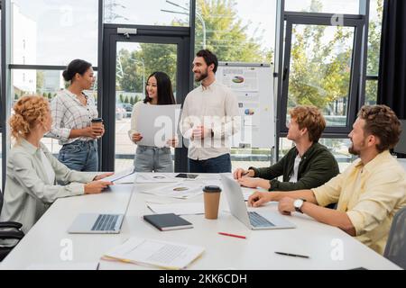 Des gens d'affaires multiethniques avec des papiers et du café qui parlent pendant la réunion au bureau Banque D'Images