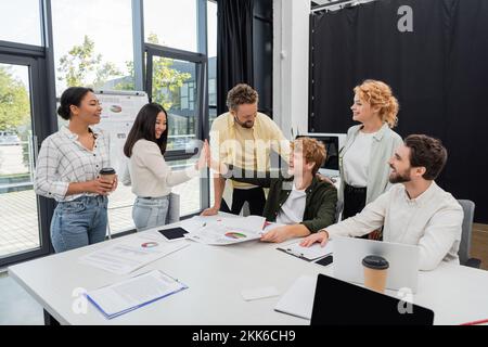 des collègues d'affaires interraciaux heureux qui offrent cinq membres de l'équipe et des infographies dans la salle de réunion Banque D'Images