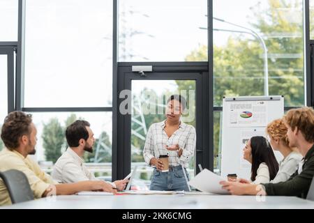 femme multiraciale avec café pour aller parler à des collègues pendant la réunion au bureau Banque D'Images