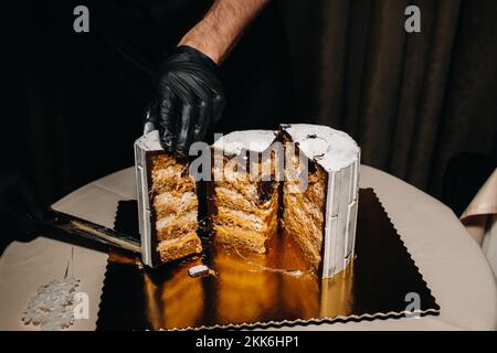 Des gâteaux incroyables. Un chef aux gloved noirs coupe un gâteau de mariage au chocolat. Le gâteau de mariage est délicieux à l'intérieur sur un fond noir.Grand gâteau en blanc Banque D'Images