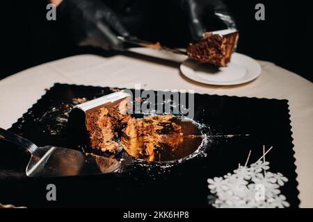 Des gâteaux incroyables. Un chef aux gloved noirs coupe un gâteau de mariage au chocolat. Le gâteau de mariage est délicieux à l'intérieur sur un fond noir.Grand gâteau en blanc Banque D'Images
