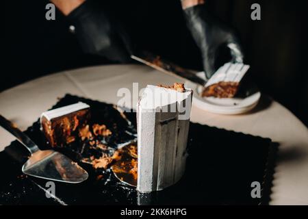 Des gâteaux incroyables. Un chef aux gloved noirs coupe un gâteau de mariage au chocolat. Le gâteau de mariage est délicieux à l'intérieur sur un fond noir.Grand gâteau en blanc Banque D'Images
