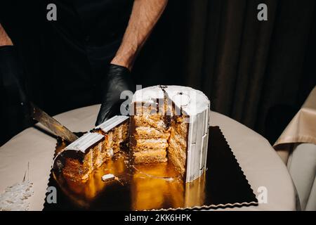 Des gâteaux incroyables. Un chef aux gloved noirs coupe un gâteau de mariage au chocolat. Le gâteau de mariage est délicieux à l'intérieur sur un fond noir.Grand gâteau en blanc Banque D'Images