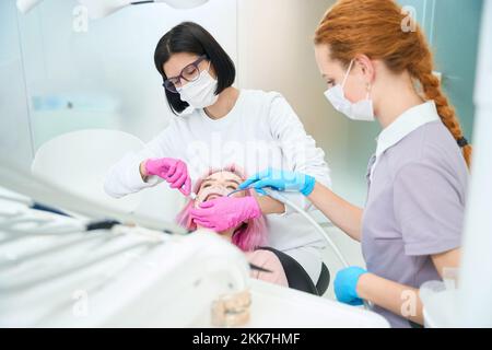 Une femme dentiste effectue une intervention dentaire à un jeune patient Banque D'Images