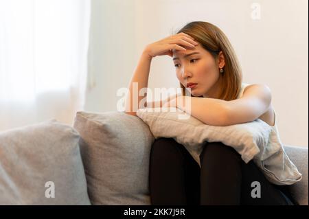 Une jeune femme asiatique se sente déprimée et malheureuse assise sur un canapé à la maison Banque D'Images