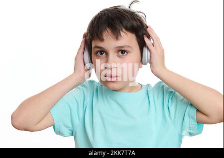 Portrait en gros plan beau garçon adolescent mettant sur un casque sans fil, regardant l'appareil photo, isolé sur fond blanc Banque D'Images