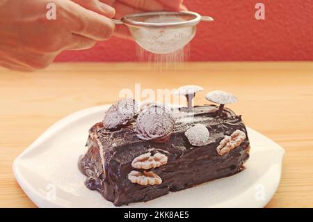 Saupoudrer à la main de sucre en poudre dans le gâteau de Noël de la Yule au chocolat fraîchement cuit Banque D'Images