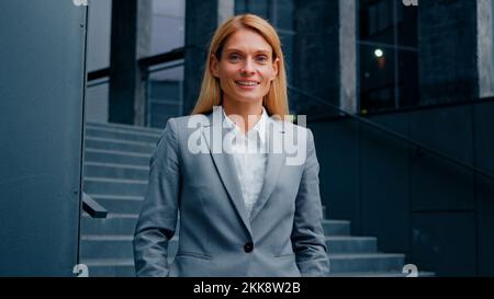 Rêveuse femme d'affaires debout près de l'immeuble de bureau regardant de côté confiante femme d'affaires chef banquier se tourne vers caméra jeune Banque D'Images