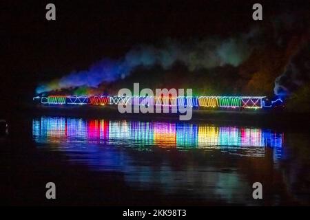 Kingswear, Devon, Royaume-Uni. 25th novembre 2022. Le train de lumière de Noël sur le chemin de fer de Dartmouth qui circule entre le 25th novembre et le 30th décembre 2022 se reflète dans l'eau calme de la rivière Dart alors qu'elle se dirige vers Paignton à Devon après avoir quitté Kingswear. Les wagons et les locomotives à vapeur du service de fête sont éclairés à l'intérieur et à l'extérieur par des lumières colorées. Crédit photo : Graham Hunt/Alamy Live News Banque D'Images