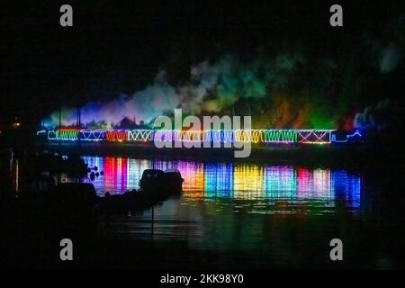 Kingswear, Devon, Royaume-Uni. 25th novembre 2022. Le train de lumière de Noël sur le chemin de fer de Dartmouth qui circule entre le 25th novembre et le 30th décembre 2022 se reflète dans l'eau calme de la rivière Dart alors qu'elle se dirige vers Paignton à Devon après avoir quitté Kingswear. Les wagons et les locomotives à vapeur du service de fête sont éclairés à l'intérieur et à l'extérieur par des lumières colorées. Crédit photo : Graham Hunt/Alamy Live News Banque D'Images