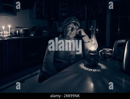 La femme triste adulte est assise à une table avec une lampe à kérosène et des meubles de cuisine en arrière-plan. Panne après l'attaque à la roquette russe Odessa Ukraine Banque D'Images