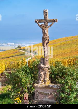 Croix chrétienne parmi les vignes aux couleurs automnales sur la colline de Turckheim - route des vins d'Alsace, France. Banque D'Images