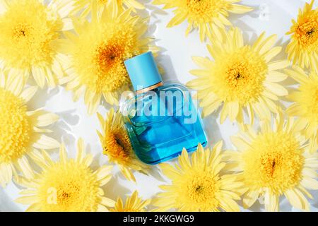 Bouteille de parfum bleue sur fond d'eau avec fleurs de chrysanthème jaunes. Vue de dessus, plan d'agencement. Banque D'Images