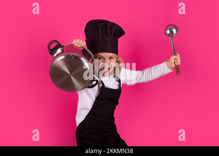 Le chef Fynny Kid cuisine avec une marmite et une louche. Enfant en uniforme de cuisinière et chapeau de chef préparant des aliments sur fond de couleur studio. Cuisine, cuisine et Banque D'Images