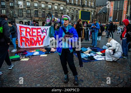 Amsterdam, pays-Bas. 25th novembre 2022. Une militante XR informe les gens par l'intermédiaire d'un mégaphone que les vêtements de seconde main derrière elle sont libres lors de la manifestation de la rébellion du Vendredi fou. L'organisation pour le climat, extinction Rebellion (XR) a organisé une manifestation contre la surconsommation pendant le Vendredi fou, et pour mettre fin à ce jour. Les activistes ont mené une action appelée Free (ky) Friday sur la place du Dam où ils ont placé des centaines de vêtements de seconde main que les gens pouvaient emporter gratuitement ou échanger des vêtements. Avec cette action l'organisation veut mettre le profit au-dessus des gens an Banque D'Images