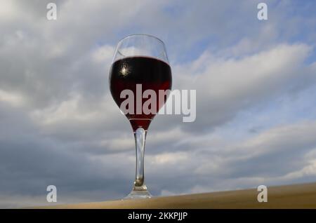 Dégustez un verre de délicieux vin rouge fruité avec un ciel nuageux d'été en arrière-plan. Banque D'Images