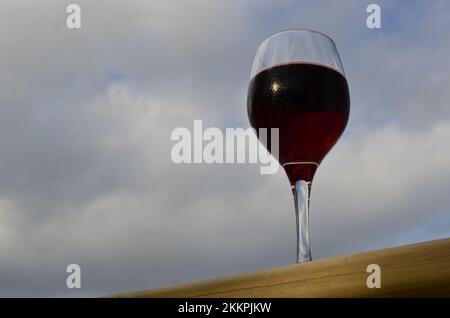 Dégustez un verre de délicieux vin rouge fruité avec un ciel nuageux d'été en arrière-plan. Banque D'Images