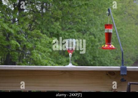 Mangeoire à vin rouge et colibris sur une rambarde en bois Banque D'Images