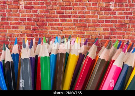 Crayons de couleur de différentes couleurs et mur de briques sur fond blanc Banque D'Images