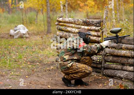 Homme joueur de tir avec un pistolet à paintball se cachant derrière un abri en bois sur un terrain de jeu dans une forêt. Banque D'Images