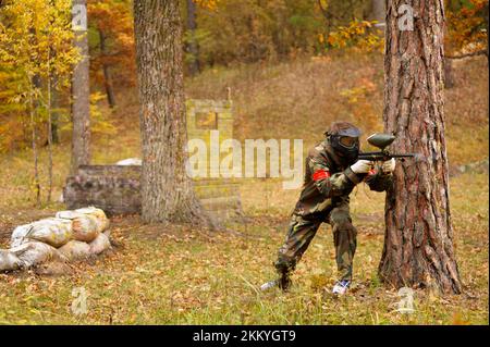 Homme joueur de tir avec un pistolet à paintball se cachant derrière l'arbre sur un terrain de jeu dans une forêt. Banque D'Images