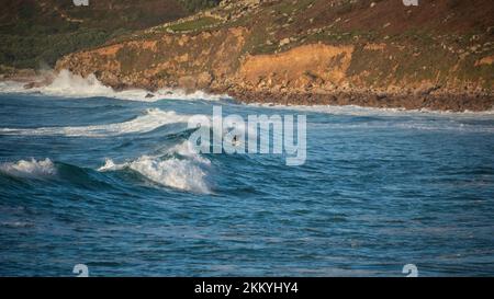 Des surfeurs non identifiés qui surfent sur les vagues à Sennen Cove, dans les Cornouailles, à la fin du coucher du soleil Banque D'Images