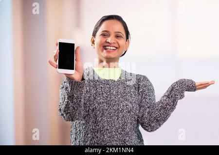 Jeune femme indienne joyeuse montrant un smartphone moderne Banque D'Images