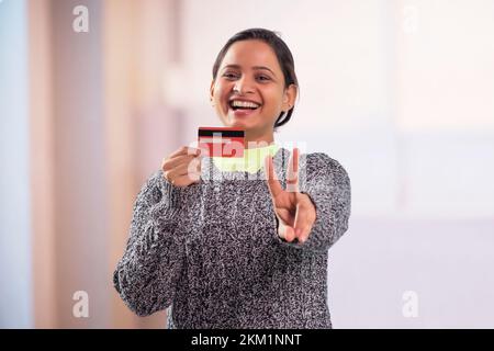 Portrait d'une jeune femme souriante montrant une carte de crédit vierge et la victoire Banque D'Images